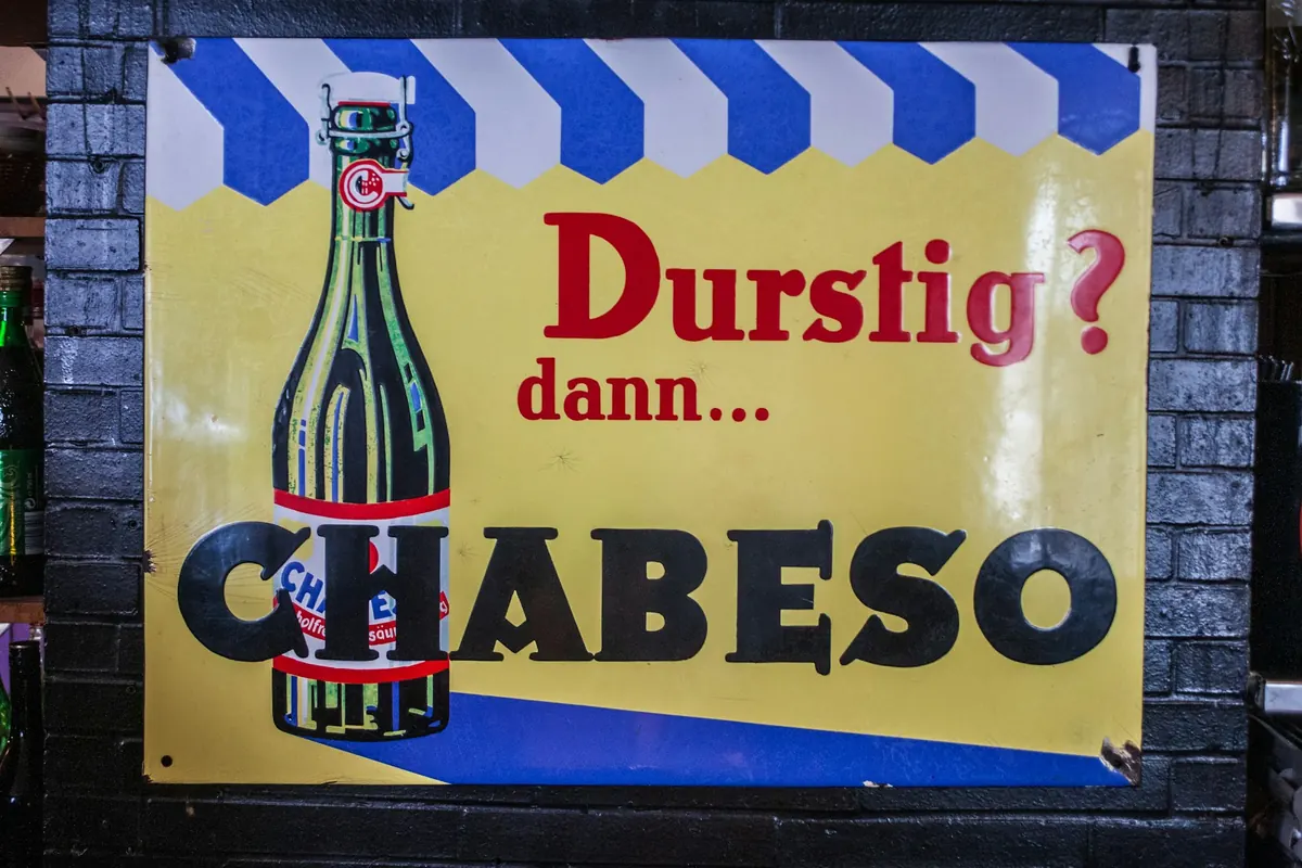 Werbeschild mit Flasche und Werbespruch an dunkler Ziegelwand