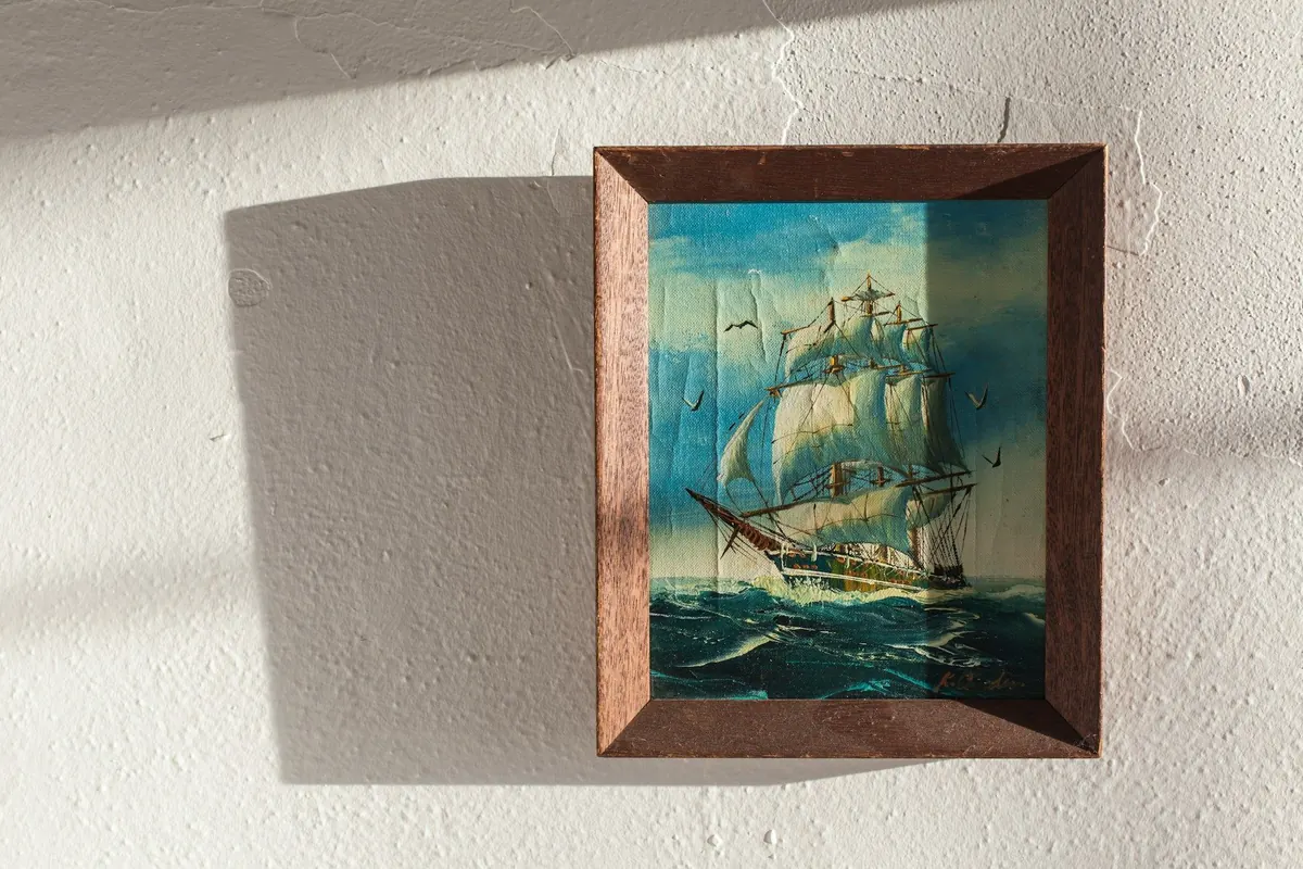 Ölbild eines Segelschiffs im Holzrahmen an weißer Wand