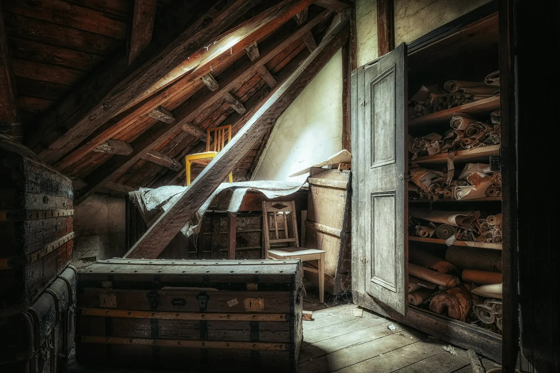 Grenier avec coffre, chaise et armoire ouverte en lumière rasante