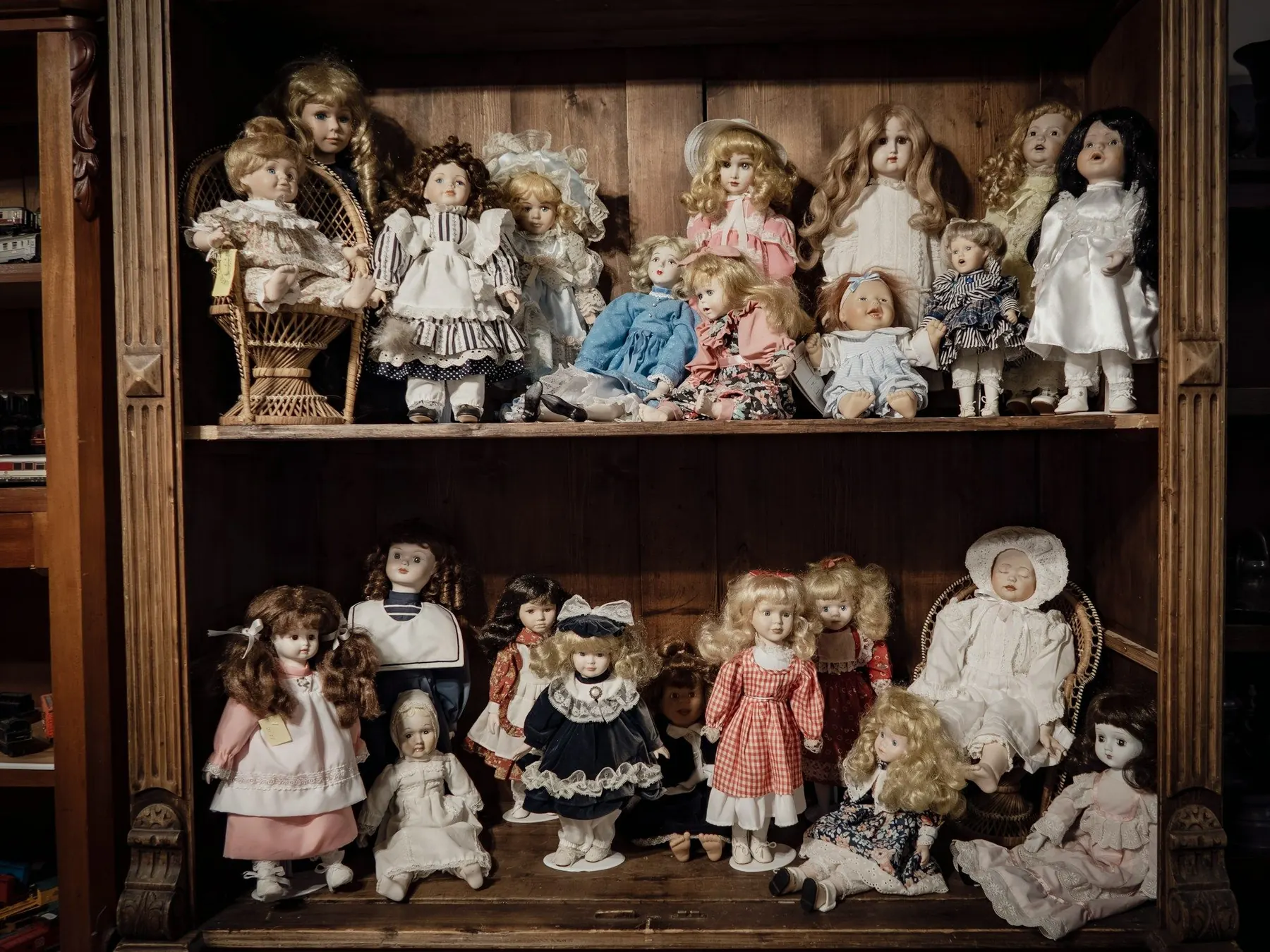 Antique dolls in dresses on two wooden shelves of a cabinet
