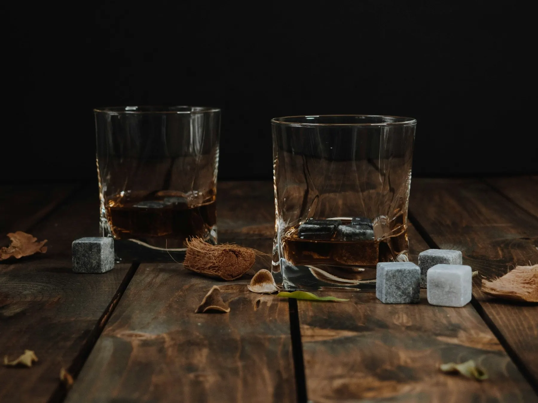 Deux verres à whisky avec des pierres à whisky sur une table en bois sombre
