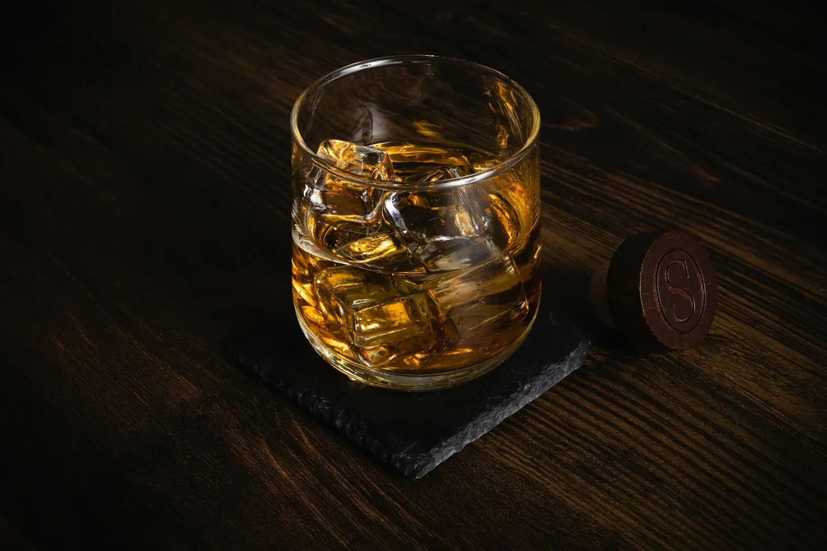 Verre de whisky avec glaçons sur un dessous-de-verre en ardoise